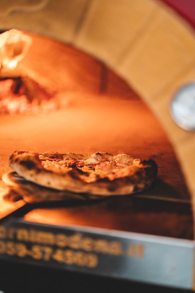 Una pizza dentro il forno a legna, sulla brace