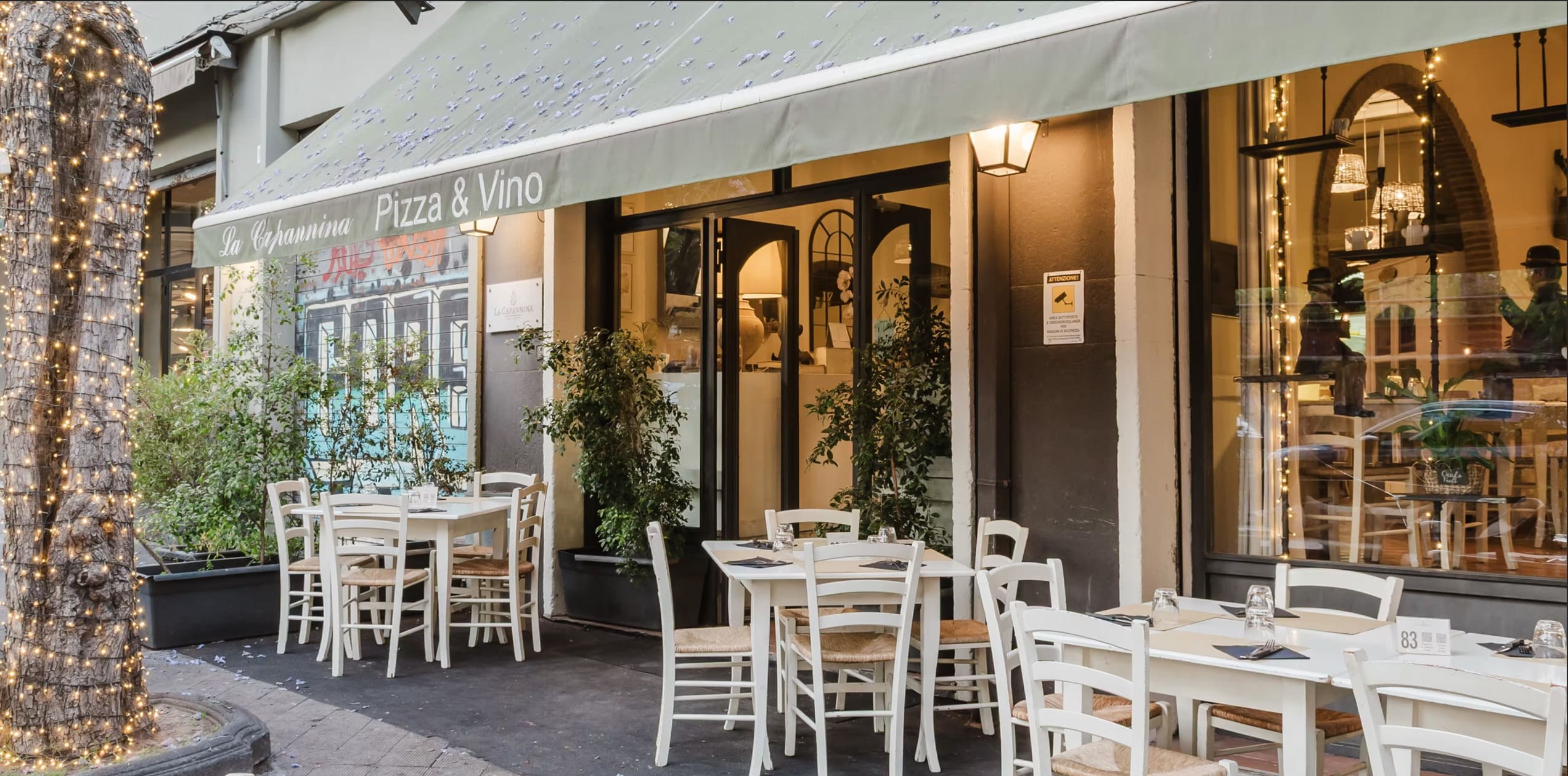 L'ingresso su Via Sant'Euplio, con la tenda Pizza e Vino e i tavoli fuori sotto la palma illuminata